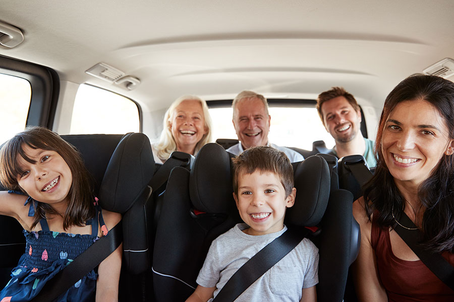 A large family sitting in the backseats of a vehicle buckled into their seats on a sunny day.